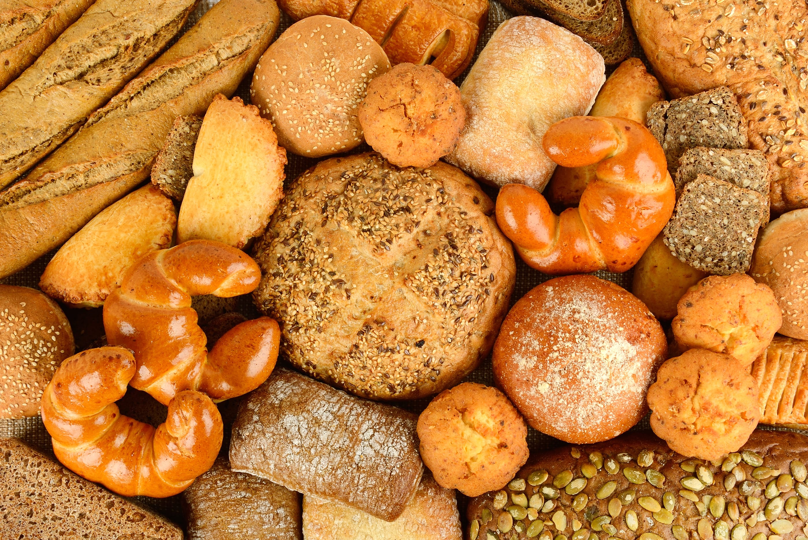 Collection of bread products (buns, baguettes, cereal bread, muffins, ciabatta, croissants) Top view.