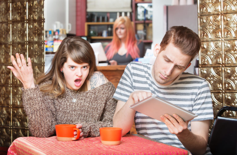 Insulted woman at table with young man using tablet